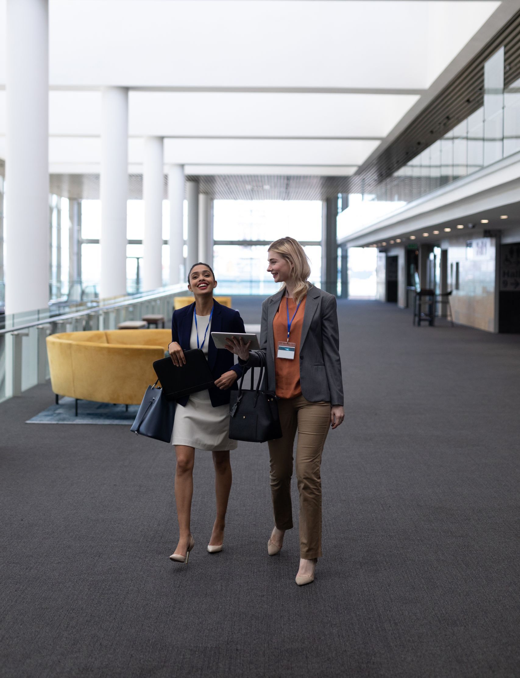 Front view of pretty young multi-ethnic businesswomen interacting with each other while walking in modern office. They are smiling